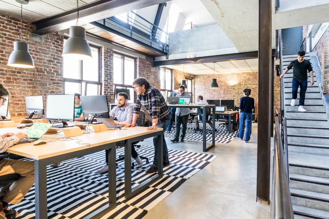 Des personnes au travail sur de longues tables dans un loft en briques