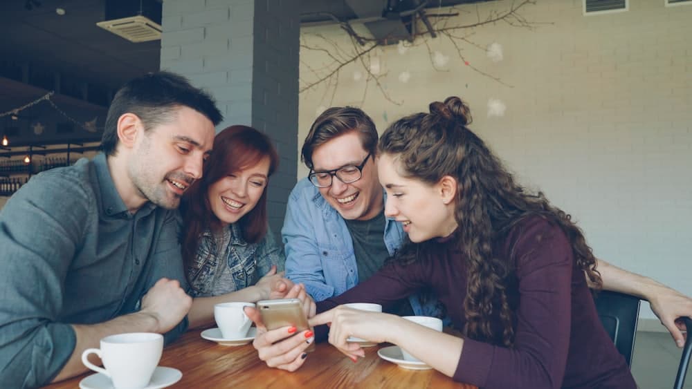 Quattro amici ridono attorno a un telefono al tavolino di un caffè