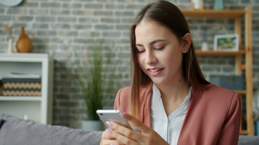 Une femme qui sourit à son téléphone dans une pièce lumineuse