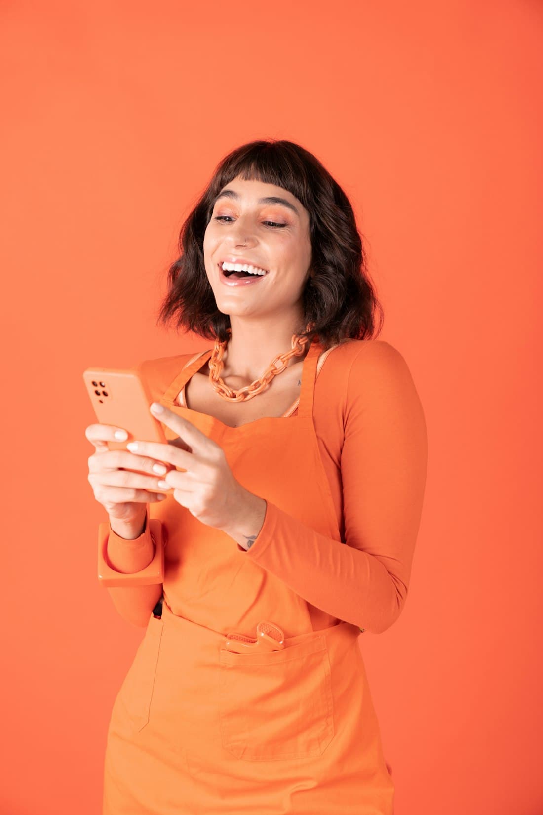 A woman laughing at her phone against an orange backdrop
