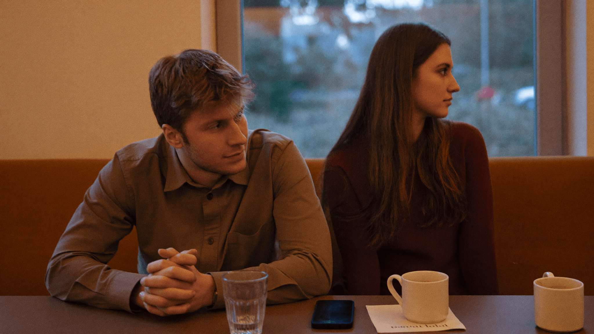 Two people sitting close together but looking in different directions — emotional distance despite physical proximity