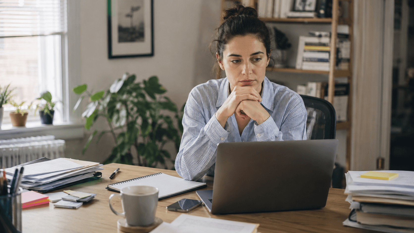 Une personne hésite avant de commencer une tâche importante sur son ordinateur portable, tandis que de petites tâches terminées sont posées sur le bureau