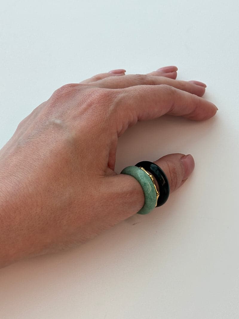 Eine Hand auf weißem Untergrund mit den dunklen und blassgrünen Steinringen, gestapelt an einem Finger