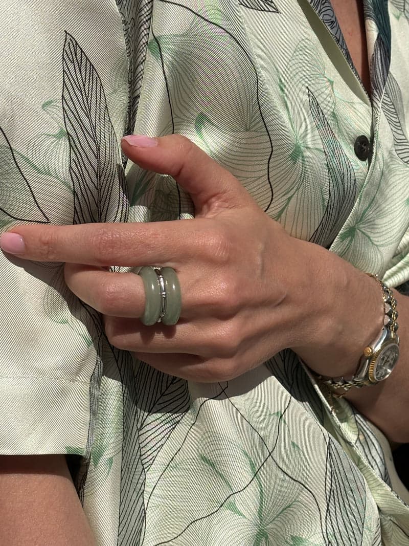 Eine Hand vor einem blassen bedruckten Seidenhemd, mit den grünen Steinringen, gestapelt an einem Finger