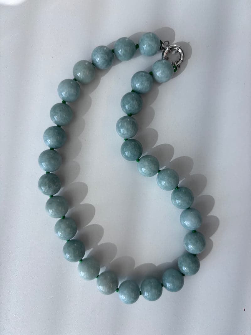 A strand of pale green round beads laid in a curve on a white surface