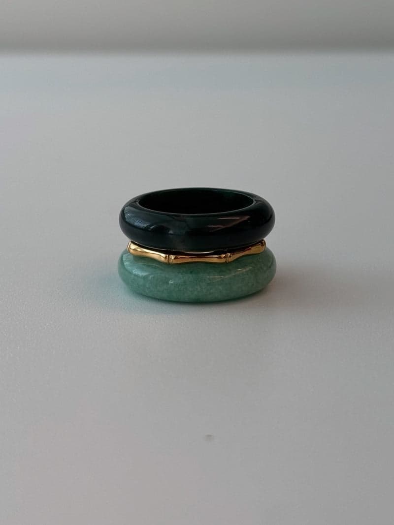 Ein gestapeltes Ringset: ein sehr dunkelgrünes Steinband oben, ein dünner goldener Ring in Bambusform, und ein blassgrünes Steinband darunter