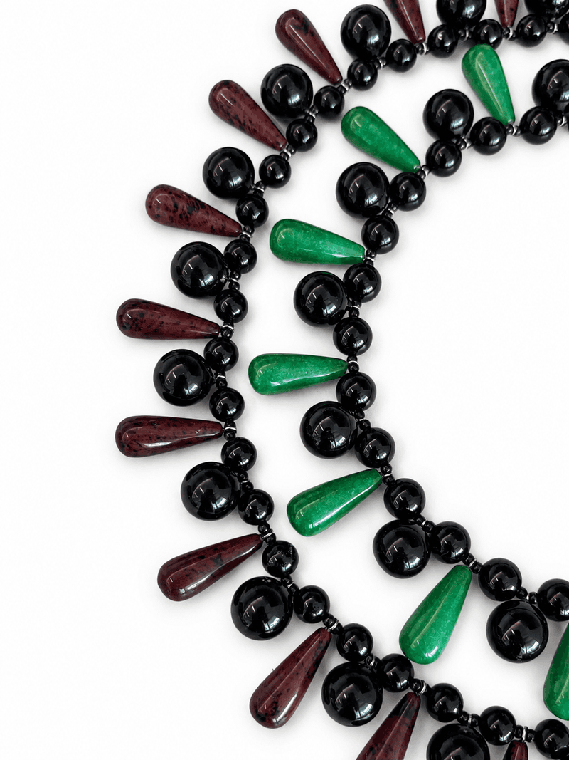 Dois colares peitorais sobrepostos, um com contas verdes em gota e outro com contas vermelho-escuras em gota, ambos com contas pretas redondas