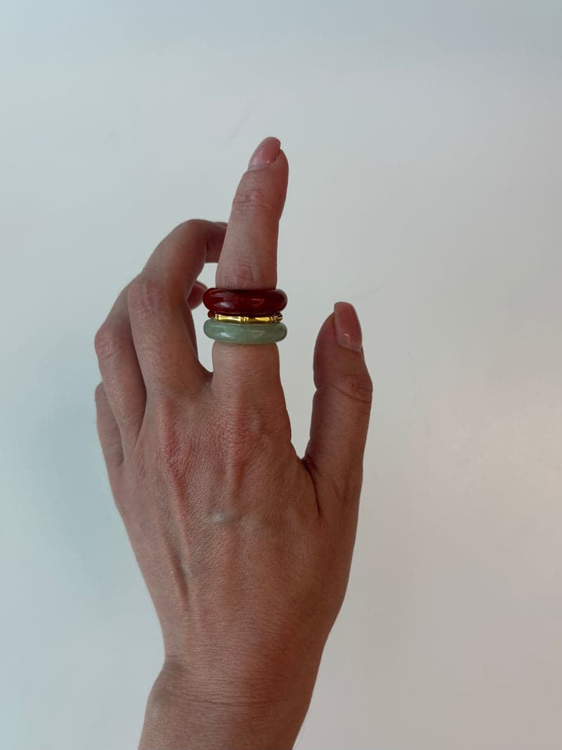 Une main levée portant les bagues en pierre rouge et vert pâle empilées à un même doigt