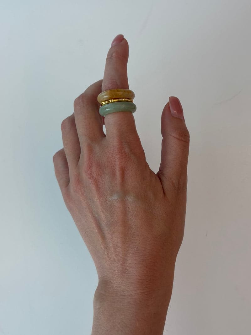 A raised hand wearing the orange and pale green stacked rings on one finger
