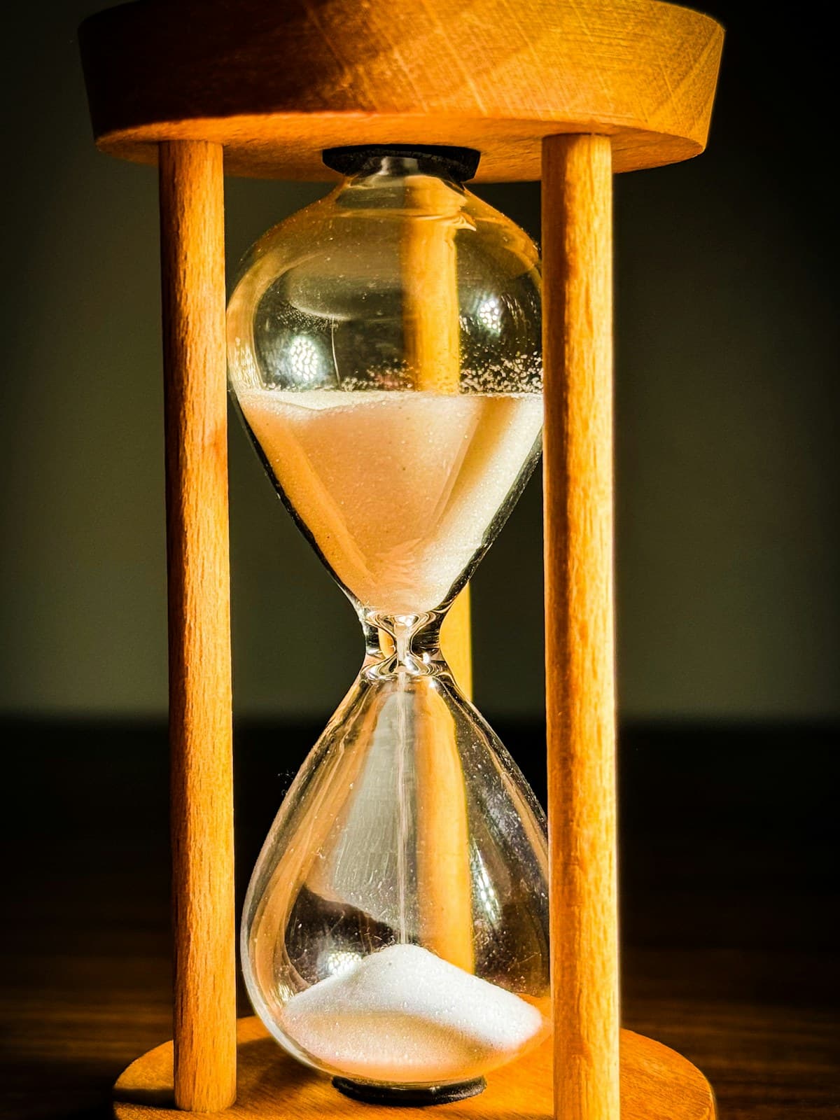 A wooden hourglass with running sand on a desk