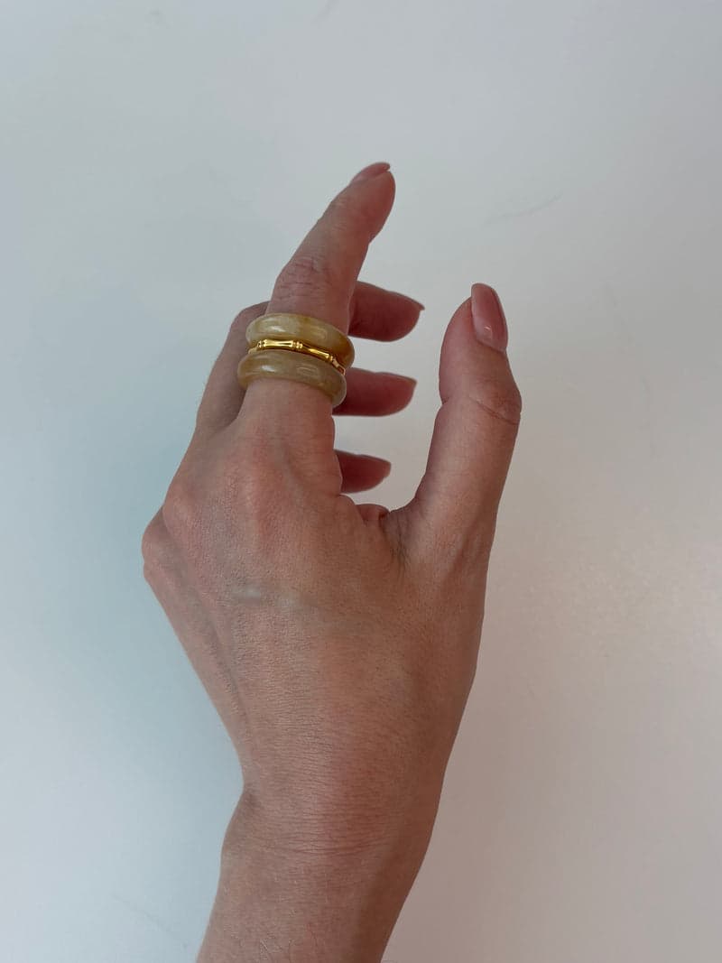 A hand wearing the pale yellow stone rings stacked on one finger