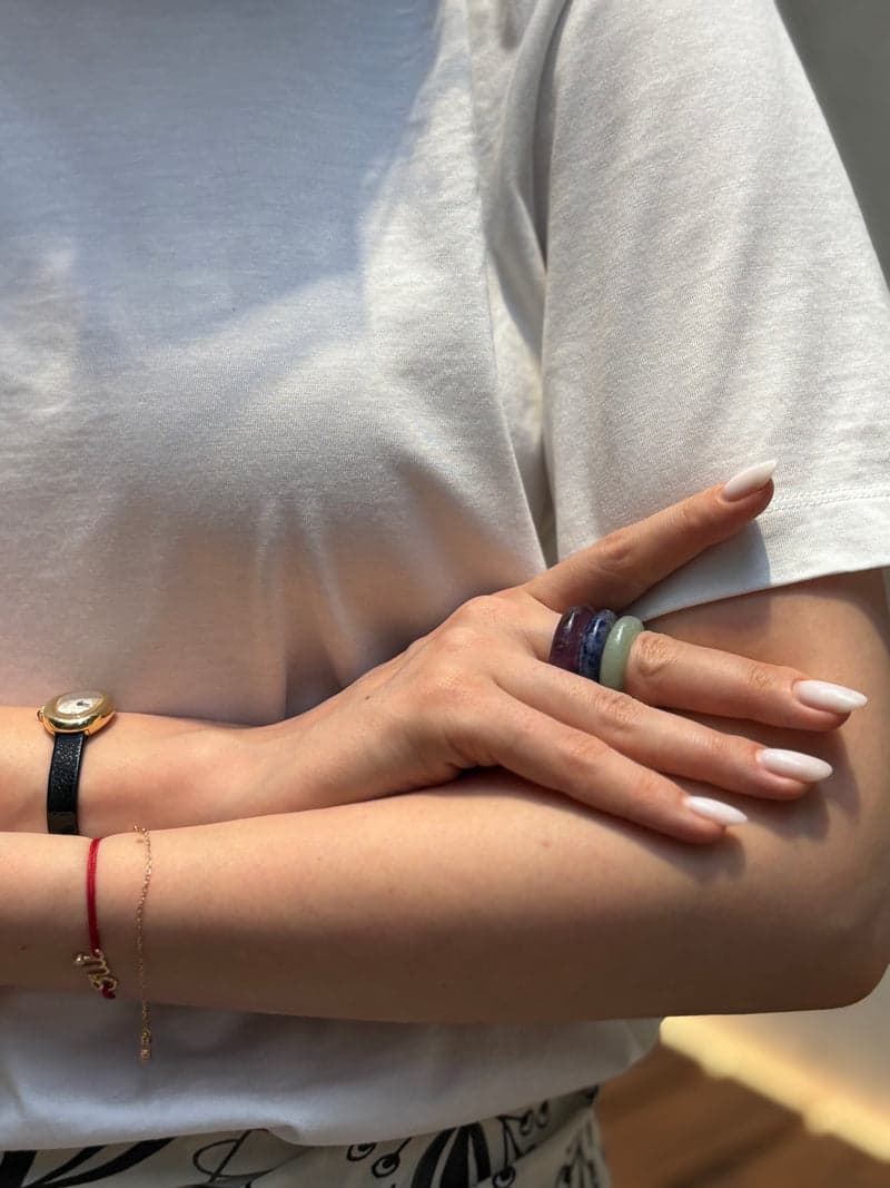 Eine Frau in einem weißen T-Shirt mit verschränkten Armen, mit den grünen, blauen und violetten Steinringen, gestapelt an einem Finger