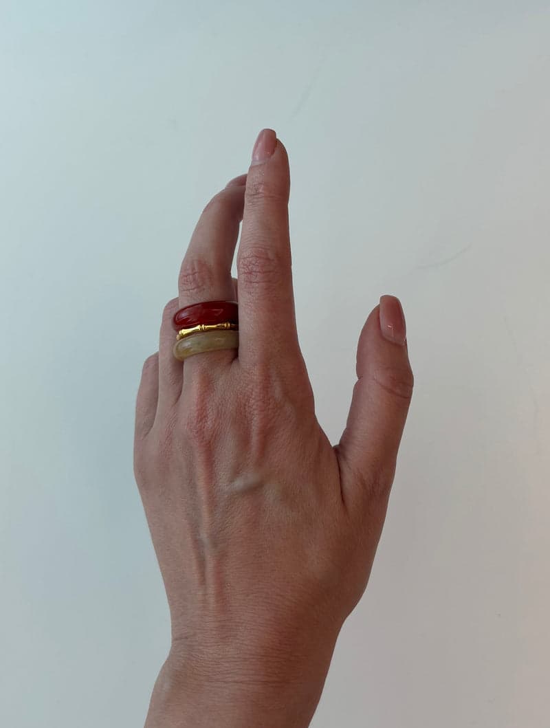 Une main levée portant les bagues en pierre rouge et jaune pâle empilées à un même doigt