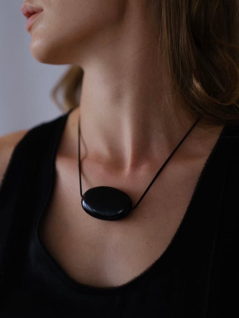 A woman in a black top wearing a single large glossy black oval pendant on a thin cord at the collarbone