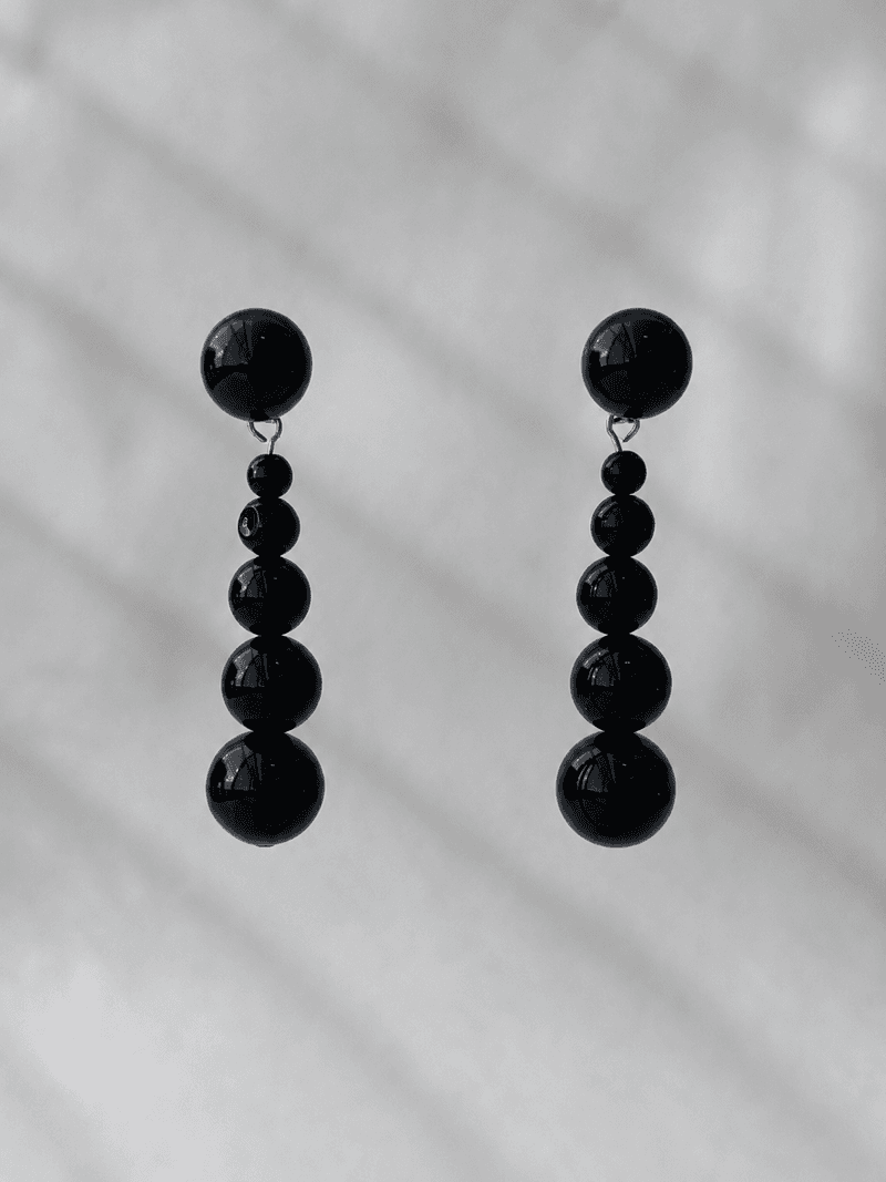 Une paire de boucles d'oreilles pendantes, chacune une ligne de perles noires brillantes allant du petit au grand