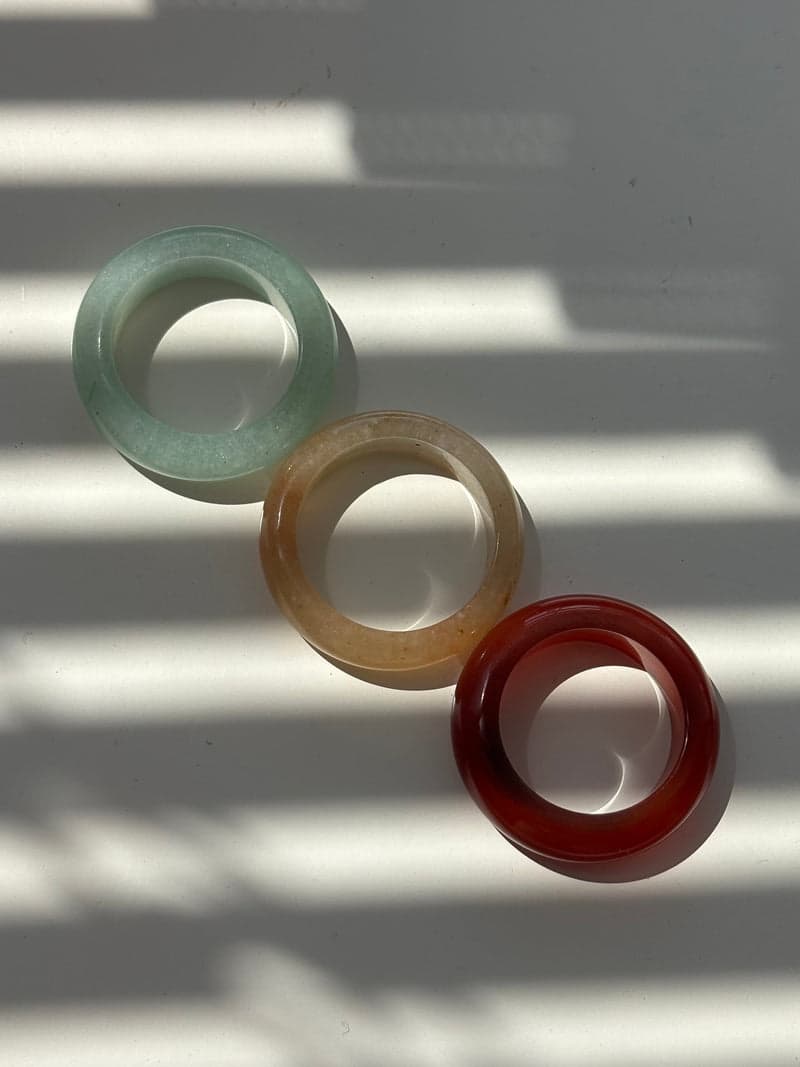 Three stone band rings laid in a diagonal line in striped window light: pale green, pale yellow and deep red