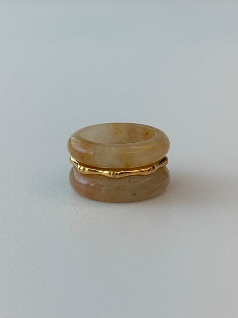 Two pale yellow stone band rings stacked with a thin gold bamboo-shaped ring between them