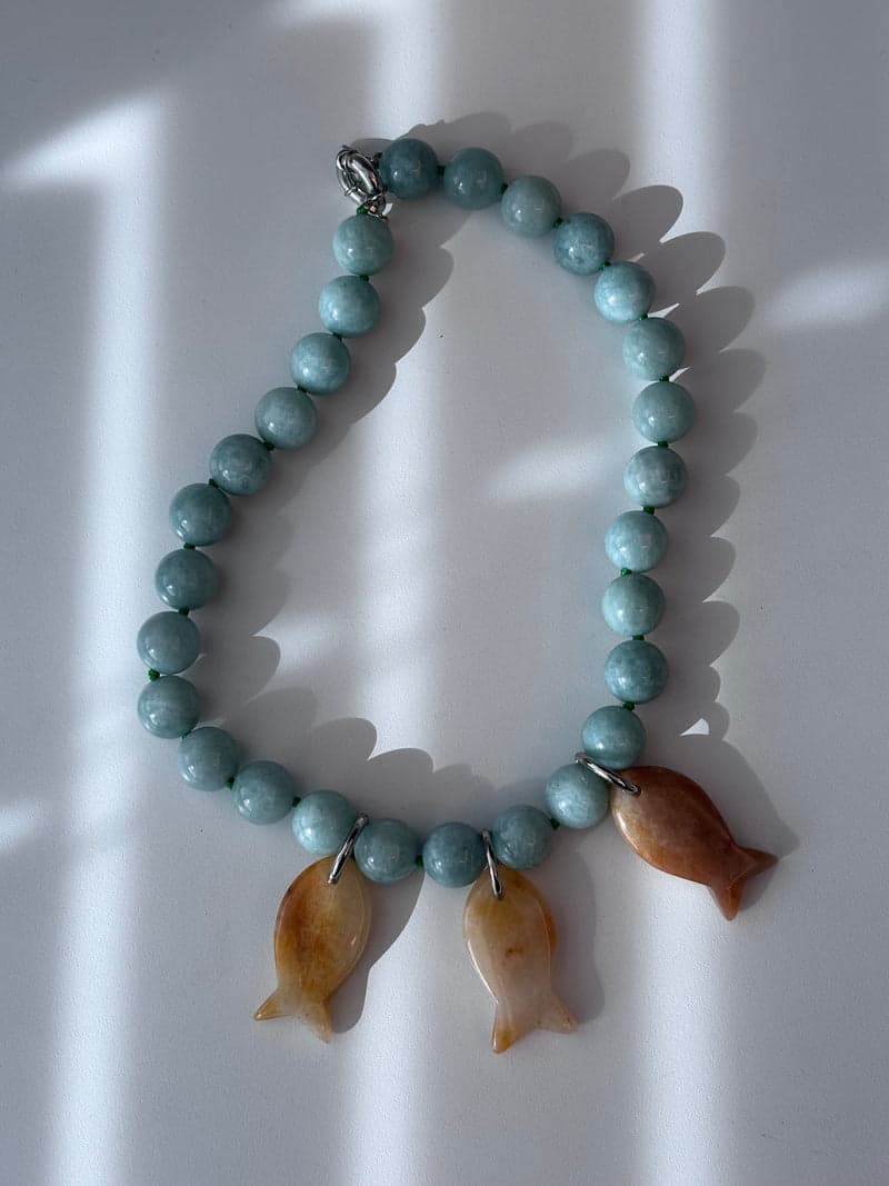 A pale green bead necklace with three small carved fish pendants in warm orange stone