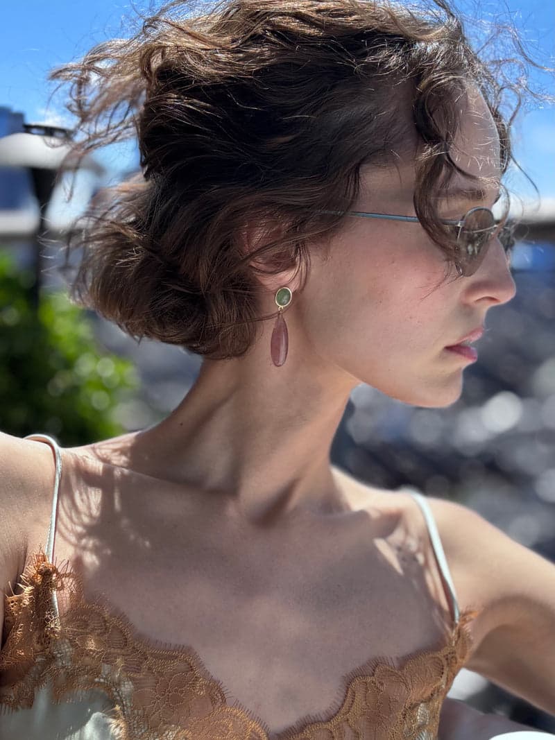 Eine Frau im Profil in hellem Sonnenlicht auf einem Dach, mit einem grünen und rosa Tropfenohrring