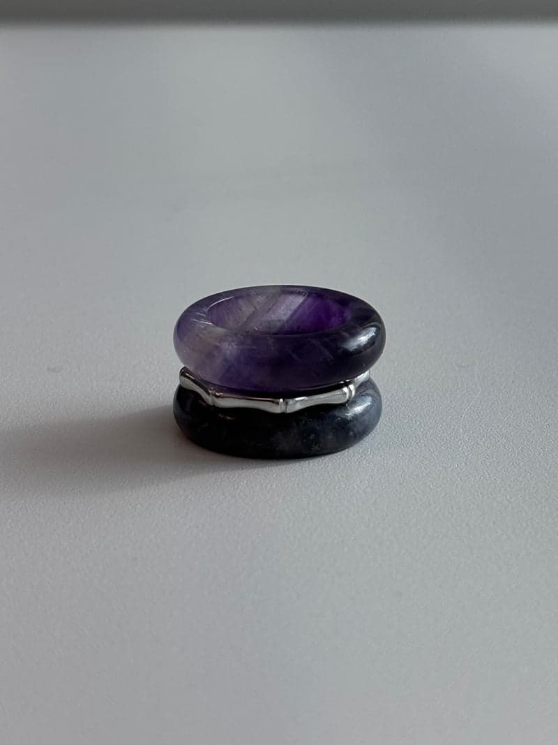 Ein gestapeltes Ringset: ein violettes Steinband oben, ein dünner silberner Ring in Bambusform, und ein dunkelblaues Steinband darunter