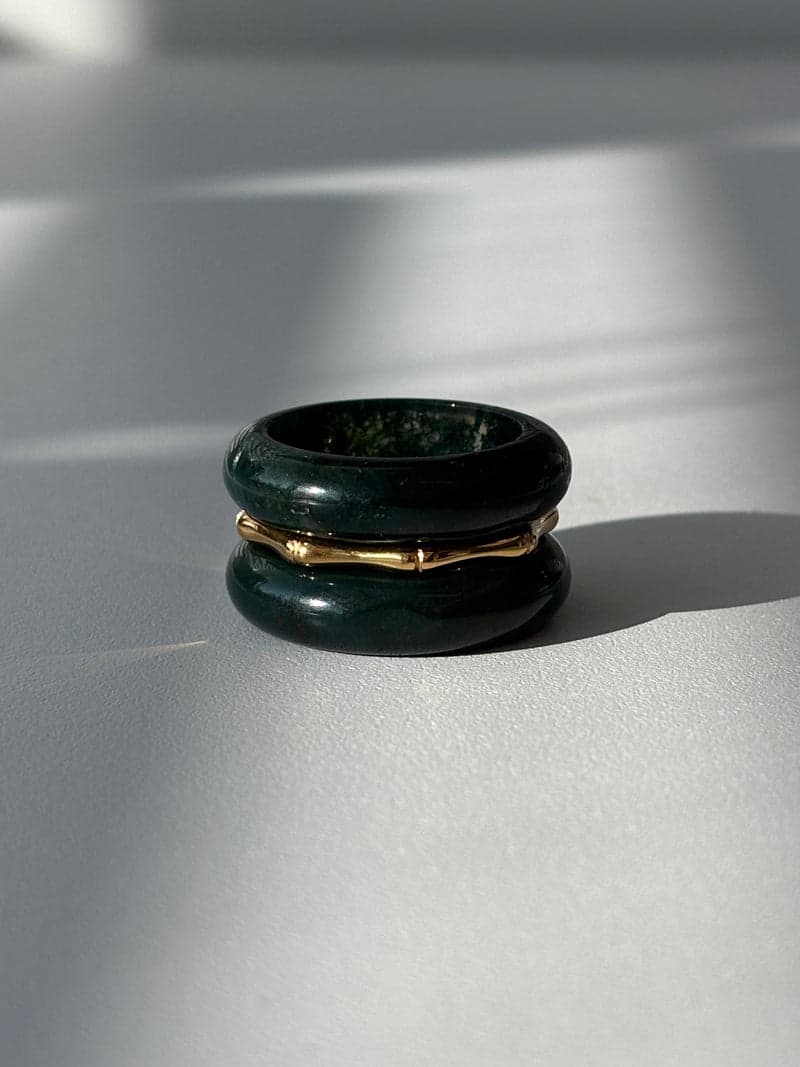 Deux anneaux en pierre vert profond empilés avec un fin anneau doré en forme de bambou entre eux, à la lumière d'une fenêtre