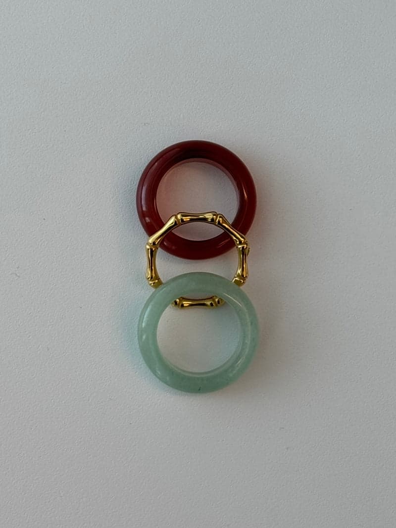 Zwei Steinringe und ein dünner goldener Ring in Bambusform, senkrecht angeordnet: ein tiefrotes Band, der goldene Ring und ein blassgrünes Band