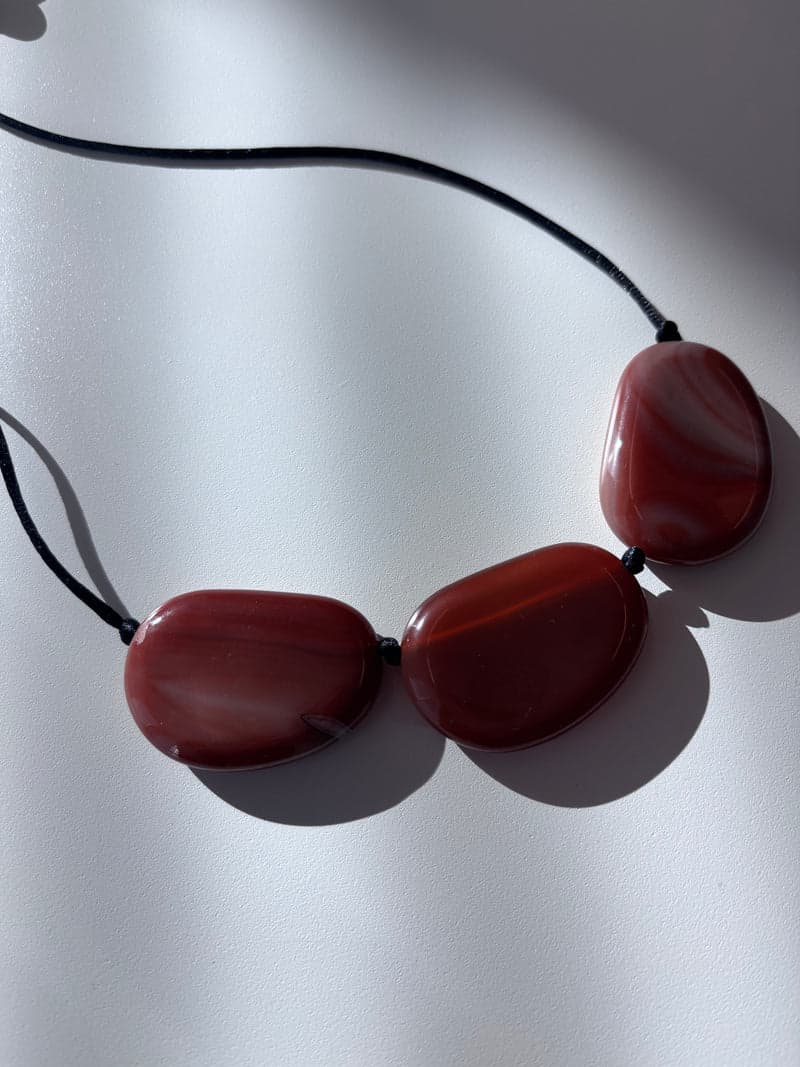 Trois grandes pierres ovales et plates, d'un brun rouge translucide avec des bandes courbes plus pâles, enfilées sur un cordon noir