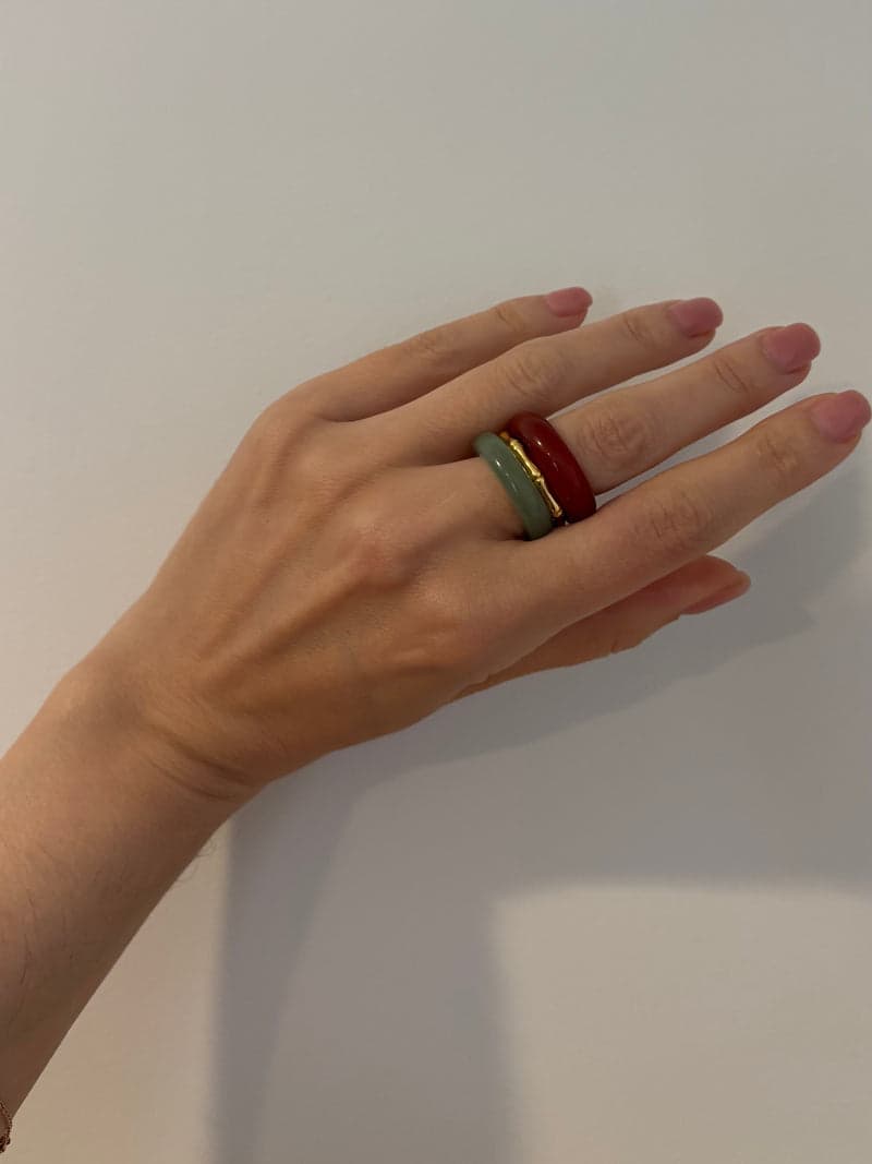Eine Hand vor einer blassen Wand mit den roten und blassgrünen Steinringen, gestapelt an einem Finger