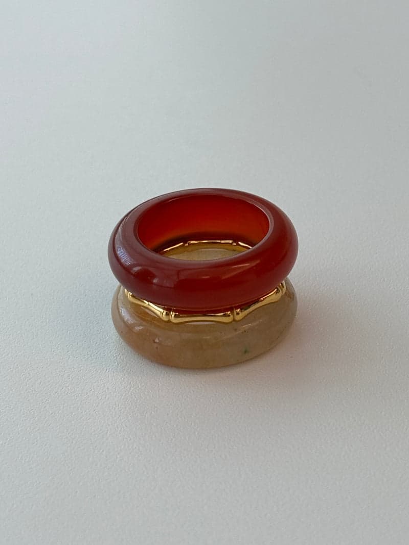 A stacked ring set: a deep red stone band on top, a thin gold bamboo-shaped ring, and a pale yellow stone band below