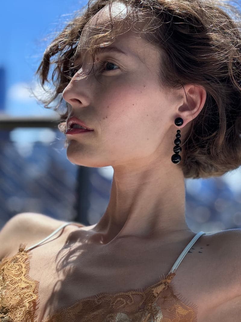 Une femme de profil en plein soleil portant une boucle d'oreille pendante en perles noires