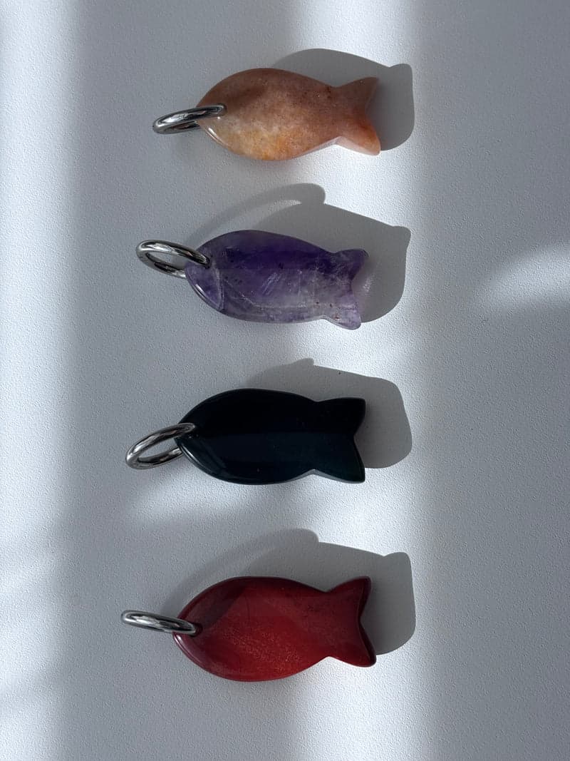 Four small carved fish pendants in a column on a white surface: orange, purple, very dark green and red