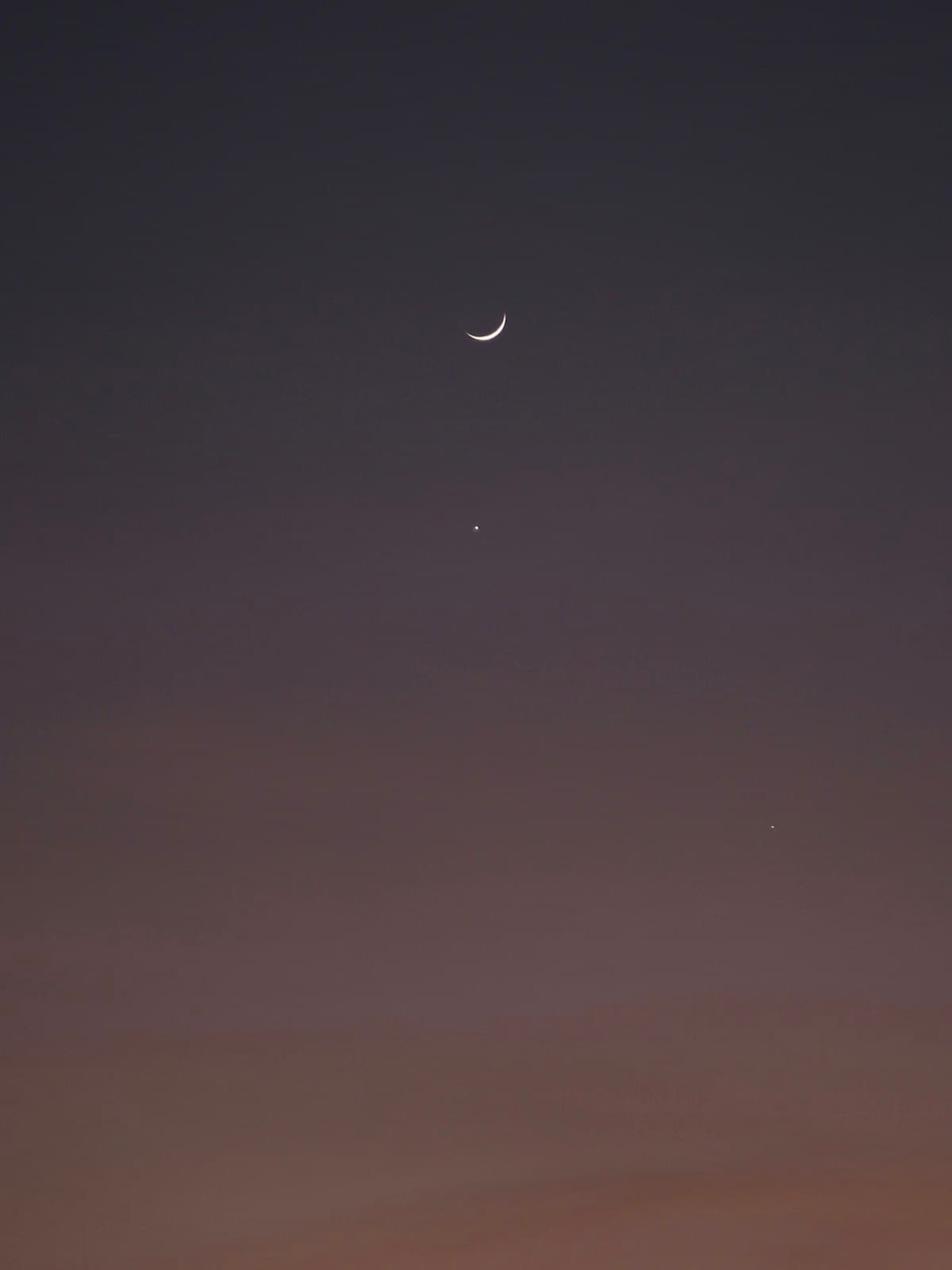 Un fin croissant de Lune avec Vénus toute proche dans un ciel crépusculaire sombre