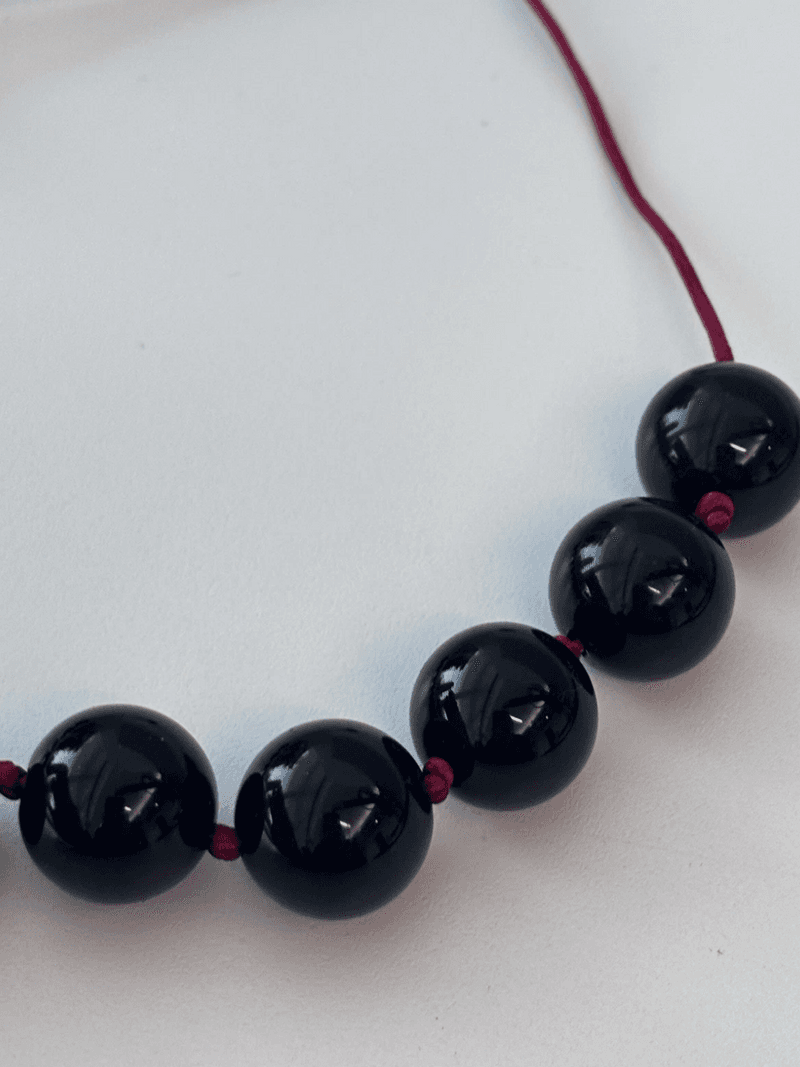 A close view of large glossy black round beads strung on a thin red cord, on a white surface