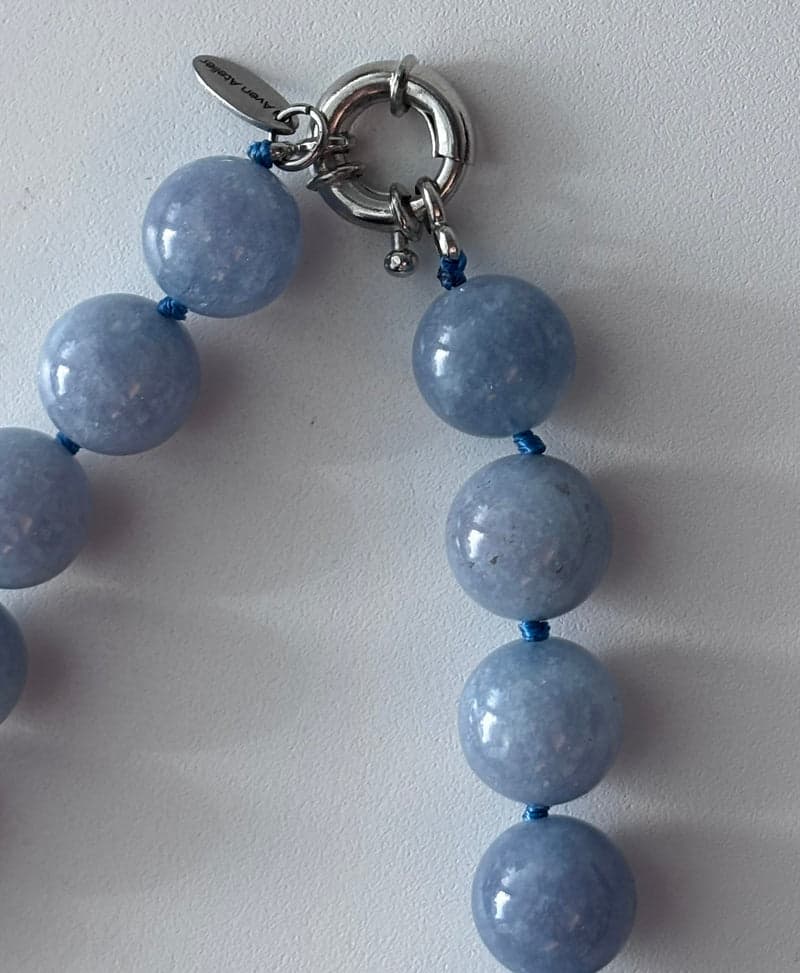 Close view of blue beads showing mottled internal texture, knotted on blue silk beside a silver clasp