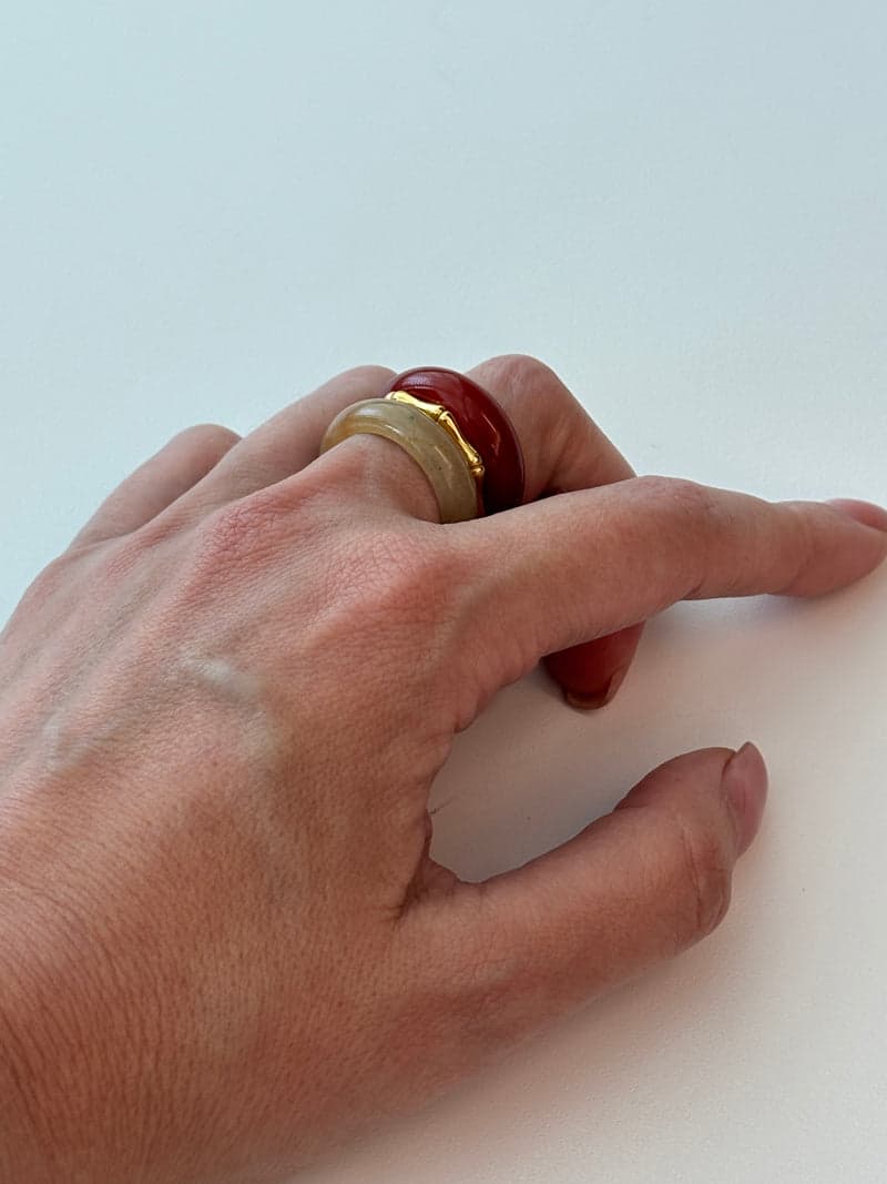 A hand resting flat wearing the red and pale yellow stacked rings on one finger