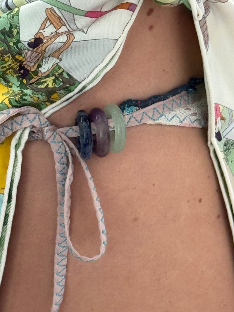 Die blauen, violetten und grünen Steinringe, aufgefädelt auf die Bindeschnur eines gemusterten Bikinis an der Hüfte
