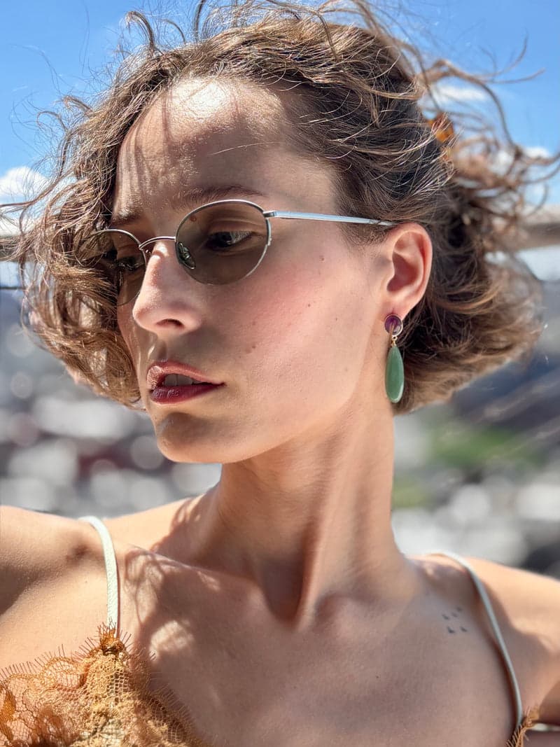 A woman in sunglasses outdoors wearing the purple and green teardrop earring