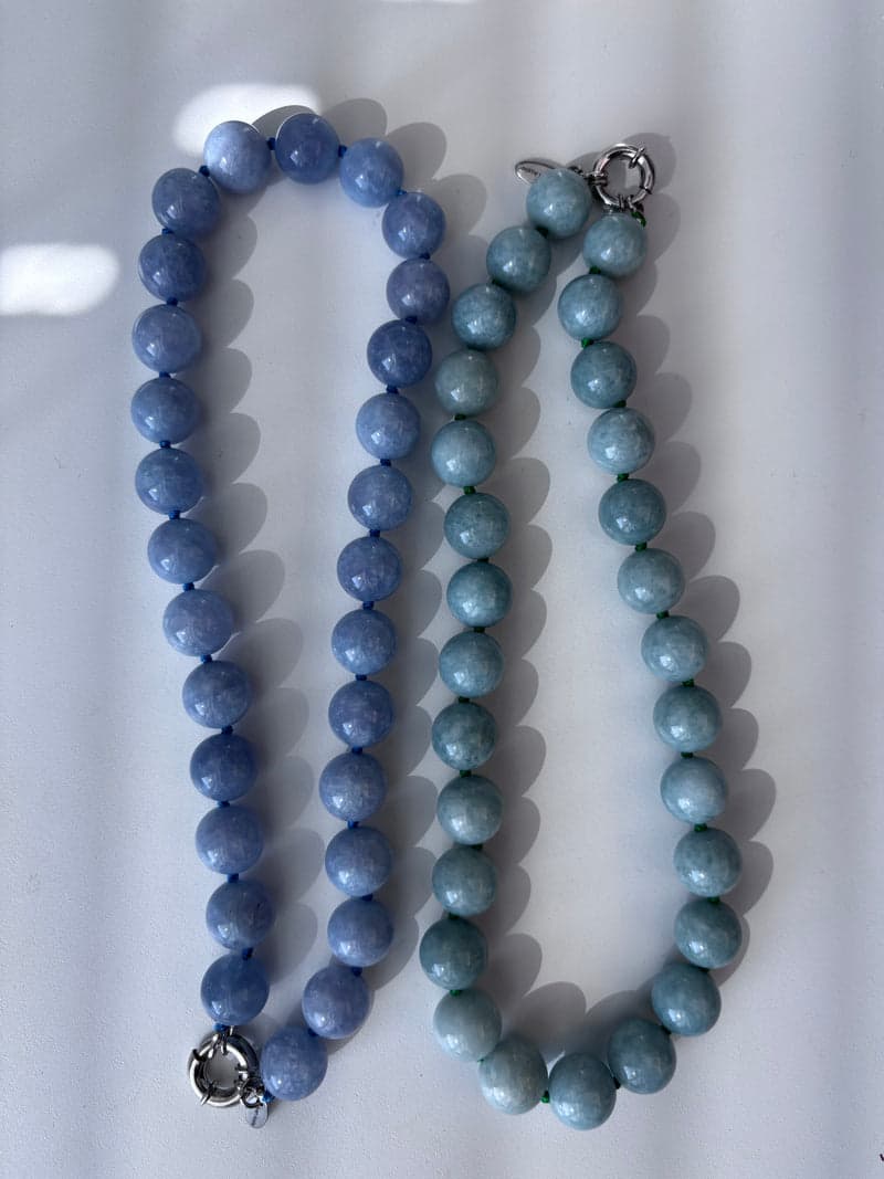 Two bead necklaces laid side by side, one in blue stone and one in pale green stone
