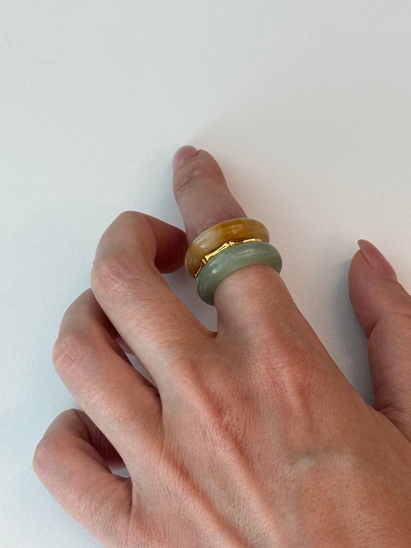 Eine Hand auf weißem Untergrund mit den orangen und blassgrünen Steinringen, gestapelt an einem Finger