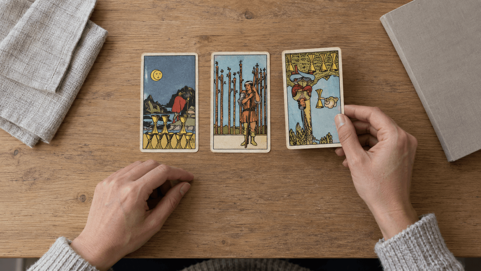 Draufsicht auf eine Person, die die dritte Karte einer Ja-Nein-Tarotlegung mit zwei aufrechten und einer umgekehrten Karte auslegt.